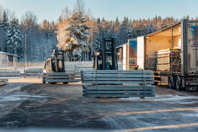 Trukit lastaavat teräsprofiileja toimitusta varten. Talvi.